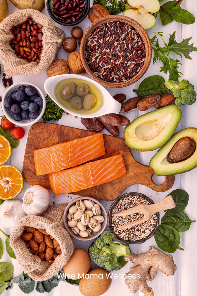 Overhead flat lay of fish, avocados, eggs, olive oil, and leafy greens on a wooden table representing nutrient-dense foods that support strong teeth.