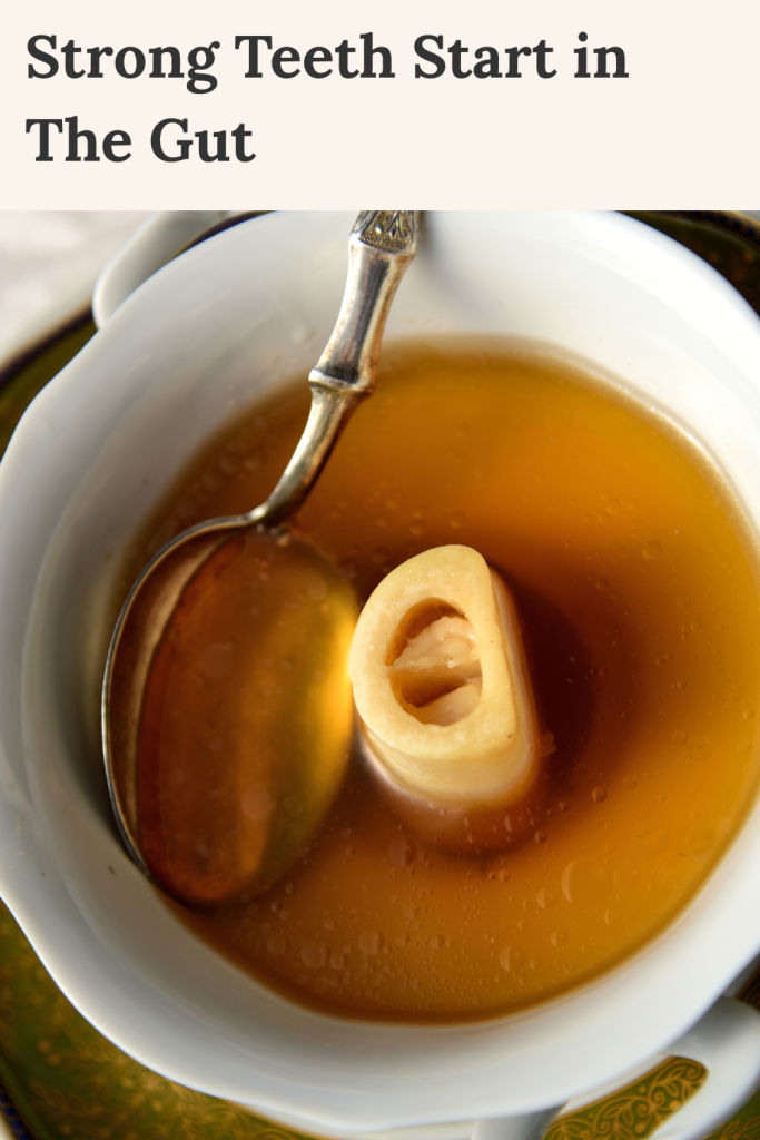 Cup of golden bone broth with a marrow bone and spoon, overlaid with text “Strong Teeth Start in the Gut."